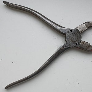 Peut inclure: Une paire de pinces vintage avec une finition argentée et une poignée noire. Les pinces ont un petit trou dans la poignée et une mâchoire dentelée.