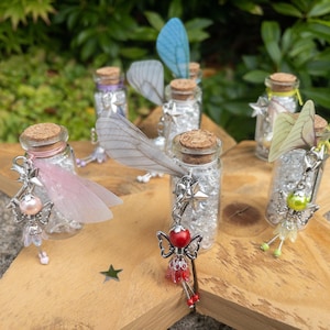 May include: Several small glass bottles with cork stoppers, filled with silver glitter. Each bottle features a fairy charm, complete with wings and star details. The bottles are displayed on a wooden, star-shaped base.
