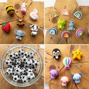 May include: A collection of silicone beads and charms featuring various shapes including a bee, gnome, swan, strawberry, highland cow, elephant, cow, frog, hippo, rainbows, footballs, penguin, star, hot air balloon, and axolotls.