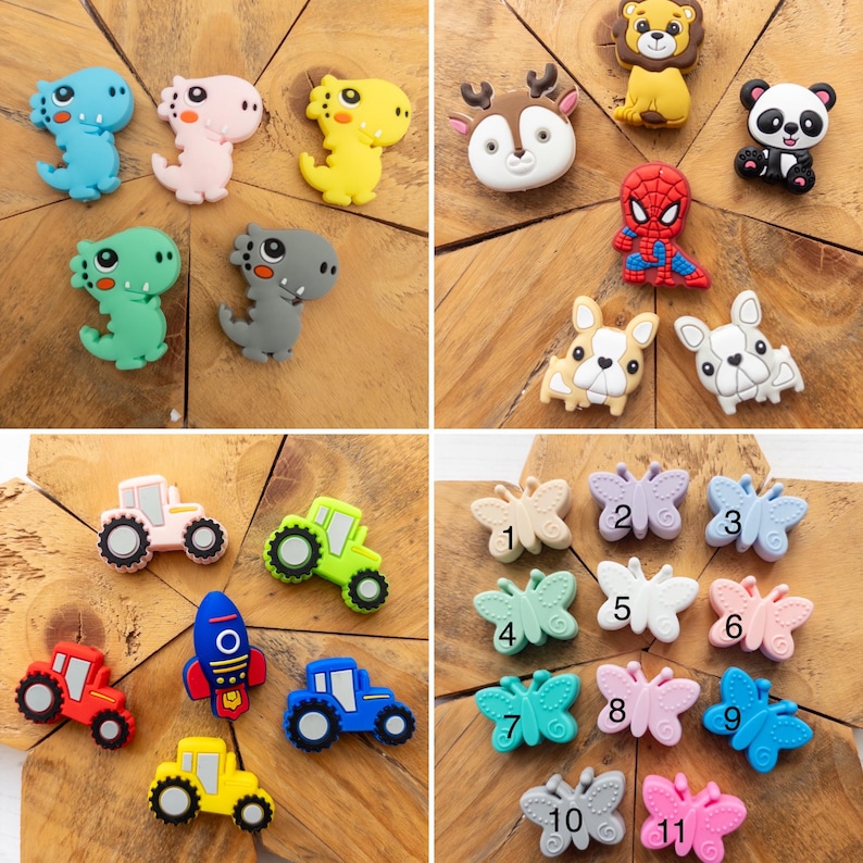 May include: A collection of silicone charms featuring various designs including dinosaurs, animals, a superhero, tractors, a rocket ship, and butterflies. The butterfly charms are numbered one through eleven in black text on their surfaces.