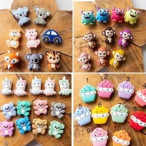 May include: A collection of silicone charms featuring various designs including koalas, monkeys, monsters, unicorns, bears, cupcakes, a fox, a tiger, and a blue car. The cupcake charms are numbered one through ten in black text.