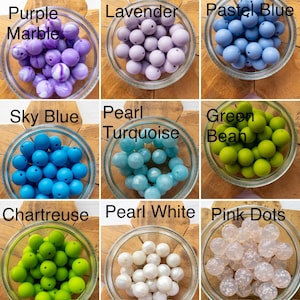 May include: A collection of nine glass bowls filled with various spherical beads labelled Purple Marble, Lavender, Pastel Blue, Sky Blue, Pearl Turquoise, Green Bean, Chartreuse, Pearl White, and Pink Dots, showcasing diverse colours and textures.