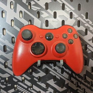 May include: A red Xbox 360 controller with black buttons and a black D-pad. The controller is on a gray and black patterned surface.