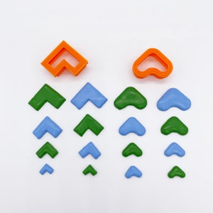 May include: A set of 15 plastic cookie cutters in three different shapes: a heart, an arrow, and a corner. The cutters are in three colors: orange, green, and blue. The cutters are arranged in a pattern on a white background.