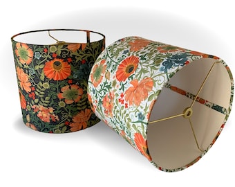 May include: Two decorative lampshades with floral patterns. One lampshade features orange flowers on a dark background, while the other has orange flowers on a white background. Both have a cylindrical shape and brass-colored metal frames.