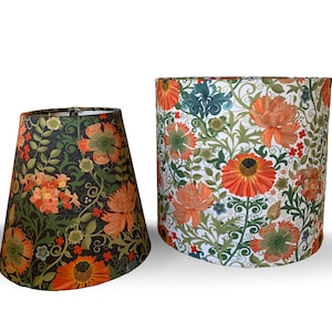 May include: Two lampshades with floral patterns. One is a tapered shape with a dark background and orange, green, and yellow flowers. The other is cylindrical with a white background and orange, green, and blue floral design. Both have a vintage aesthetic.