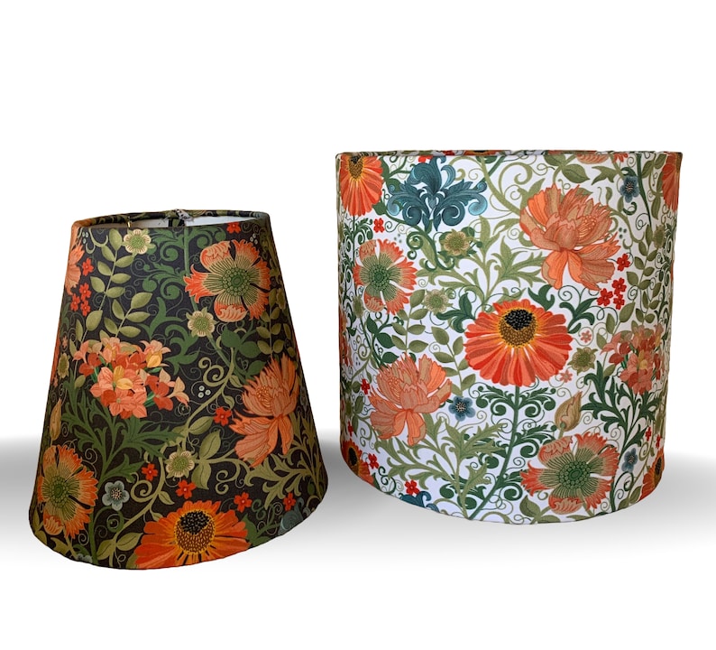 May include: Two lampshades with floral patterns. One is a tapered shape with a dark background and orange, green, and yellow flowers. The other is cylindrical with a white background and orange, green, and blue floral design. Both have a vintage aesthetic.
