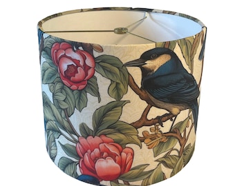 May include: Cylindrical lampshade featuring a detailed illustration of a bird perched on a branch, surrounded by red flowers and green leaves. The background is a cream color with a subtle pattern. The lampshade has a gold-colored metal frame.