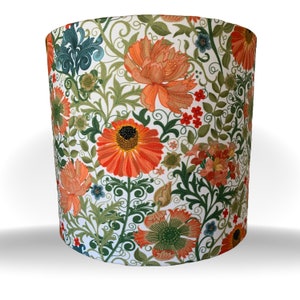 May include: Cylindrical lampshade featuring a vibrant floral pattern. The design includes large orange flowers with dark centers, green leaves, and smaller red and blue floral accents, all set against a white background. The lampshade is a decorative lighting element.