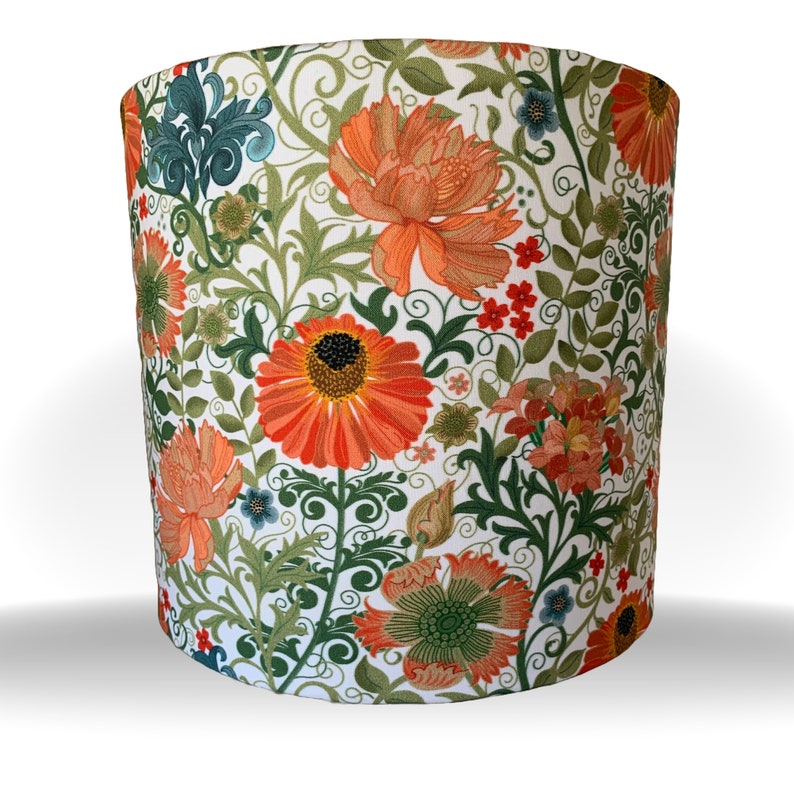 May include: Cylindrical lampshade featuring a vibrant floral pattern. The design includes large orange flowers with dark centers, green leaves, and smaller red and blue floral accents, all set against a white background. The lampshade is a decorative lighting element.