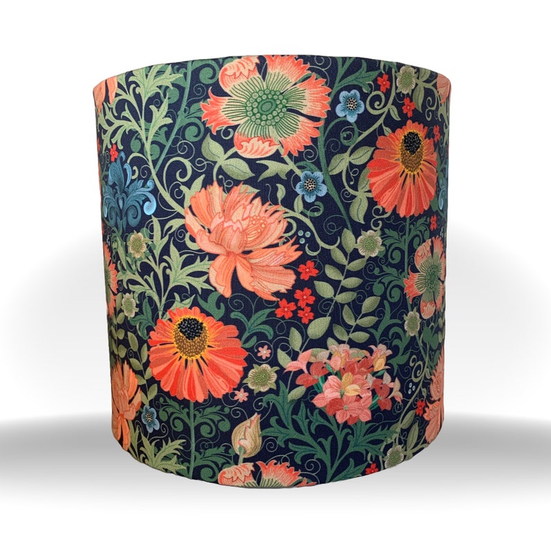 May include: Cylindrical lampshade with a dark blue background and a floral pattern. The design features large orange and pink flowers, green leaves, and smaller blue and red blossoms. The lampshade is a decorative lighting element.