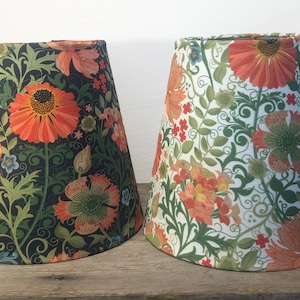 May include: Two lampshades with floral patterns. One shade has a dark background with orange and green flowers. The other shade has a white background with orange and green flowers. Both shades have a conical shape.