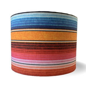 May include: Cylindrical lampshade with a vibrant, colorful striped pattern. The design features horizontal bands of blue, orange, red, and white, creating a bold and eye-catching aesthetic. This lampshade is a decorative lighting element.