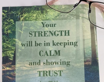 Puede incluir: Una tarjeta cuadrada con una escena de bosque y el texto "Your STRENGTH will be in keeping CALM and showing TRUST - Isa. 30:15." Gafas con montura negra descansan sobre la tarjeta.