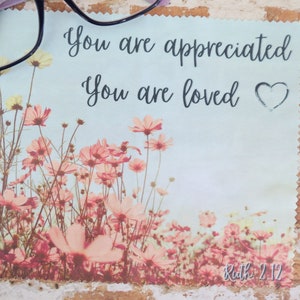 May include: A light blue microfiber cleaning cloth with a floral design and the text "You are appreciated. You are loved." with a heart symbol. The bottom of the cloth has the text "Ruth 2:12".