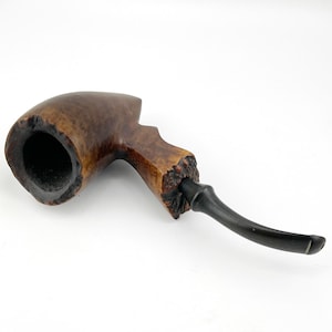 May include: A wooden tobacco pipe with a curved, dark-colored stem. The bowl is a light brown with darker wood grain, and the stem is black. The pipe is angled, showing the bowl's opening.