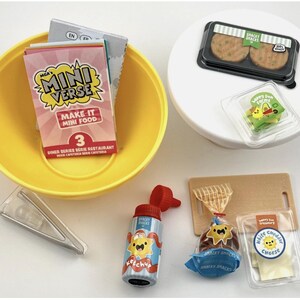 May include: A collection of miniature food items, including a yellow bowl with a Mini Verse box, a ketchup bottle, a cutting board, and packaged snacks. The snacks include burgers, cheese, and a wrapped pastry.