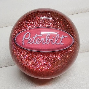 May include: Red glitter resin gear shift knob with a pink Peterbilt logo.