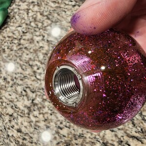 May include: A pink and black glitter filled clear resin gear shift knob with a silver threaded insert.