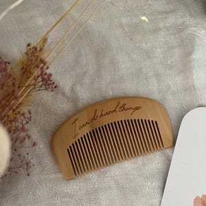 Small hand held wooden comb for natural childbirth and natural pain relief. Birth comb is on a birth alter for new baby with dried flowers. Comb is on a white cloth  engraved with the birth affirmation "I can do hard things"
