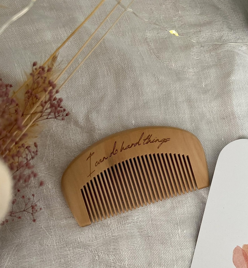 Small hand held wooden comb for natural childbirth and natural pain relief. Birth comb is on a birth alter for new baby with dried flowers. Comb is on a white cloth  engraved with the birth affirmation "I can do hard things"