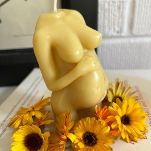 Beeswax candle in the form of a pregnant woman holding her belly is unlit on a birth altar, surrounded by books for childbirth and calendula, an herb known for its healing support