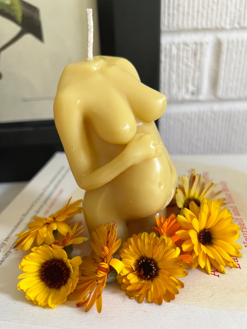 Beeswax candle in the form of a pregnant woman holding her belly is unlit on a birth altar, surrounded by books for childbirth and calendula, an herb known for its healing support