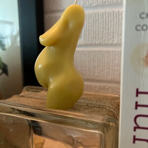 Beeswax candle in the form of a pregnant woman with huge belly is unlit on a birth altar, surrounded by labor books and 4th trimester support. Side view of womb and torso