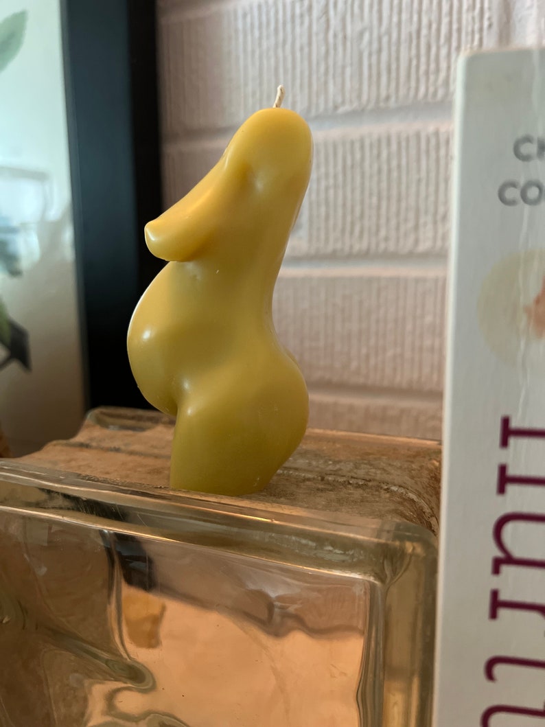 Beeswax candle in the form of a pregnant woman with huge belly is unlit on a birth altar, surrounded by labor books and 4th trimester support. Side view of womb and torso