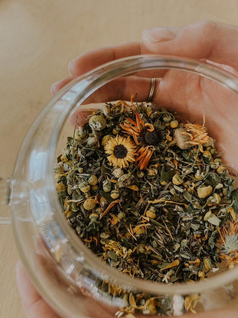 Jar of herbs for new mom healing from childbirth. Jar is held in the palms of a woman. Glass tea jar holding sitz bath herbs