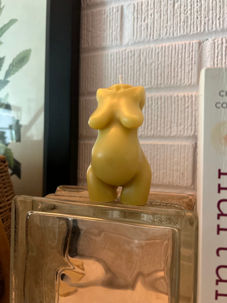 Beeswax candle in the form of a pregnant woman with huge belly is unlit on a birth altar, surrounded by labor books and 4th trimester support. white wick, tan skin candle