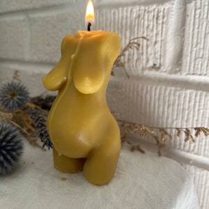 A yellow beeswax candle shaped like a pregnant woman.  The candle is lit and has a small flame on top.