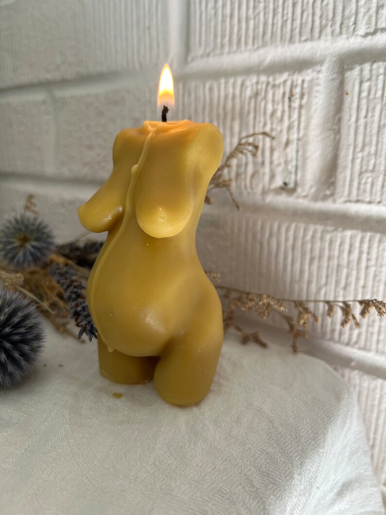 A yellow beeswax candle shaped like a pregnant woman.  The candle is lit and has a small flame on top.