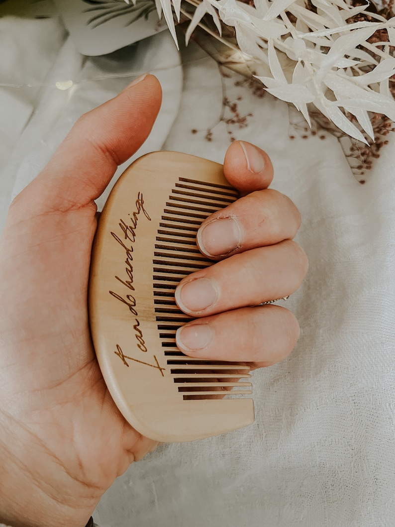 Natural birth comb held in mother's hand displaying the saying I can do hard things lifted up above a birth alter with fairy lights dried flowers and a neutral blanket