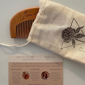 A birth comb is halfway out of it's carrying bag. The bag is engraved with a clover logo. Under the comb is a how-to card for using the comb.