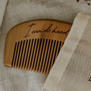 Small hand held wooden comb for natural childbirth and natural pain relief. Birth comb is coming out of a white cotton carrying bag. Comb is on a white cloth in shadow with the birth affirmation "I can do hard things"
