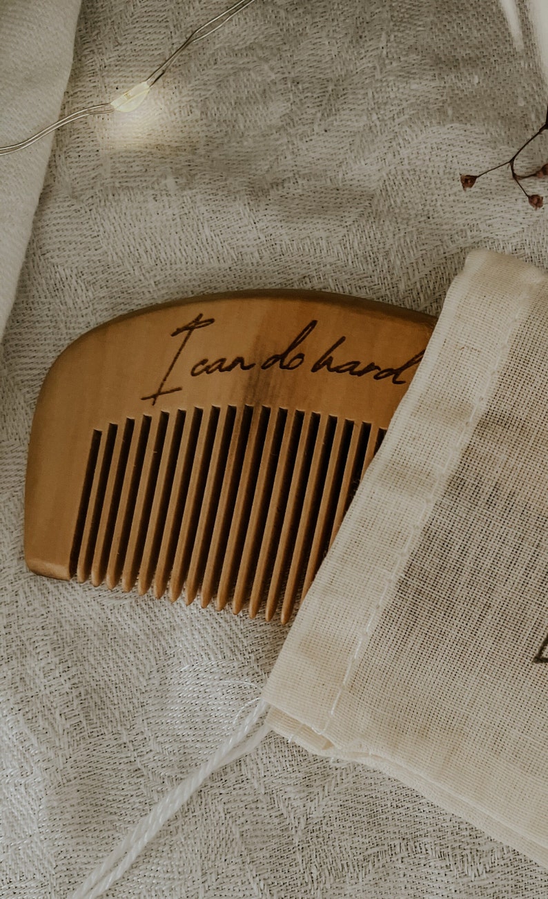 Small hand held wooden comb for natural childbirth and natural pain relief. Birth comb is coming out of a white cotton carrying bag. Comb is on a white cloth in shadow with the birth affirmation "I can do hard things"