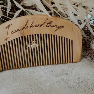 Tan labor comb with I can do hard things engraved. Small comb for hand held during birth. Resting in front of dried sage and flowers
