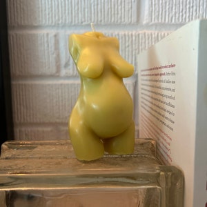 Beeswax candle in the form of a pregnant woman with belly is unlit on a birth altar, surrounded by labor books and 4th trimester support
