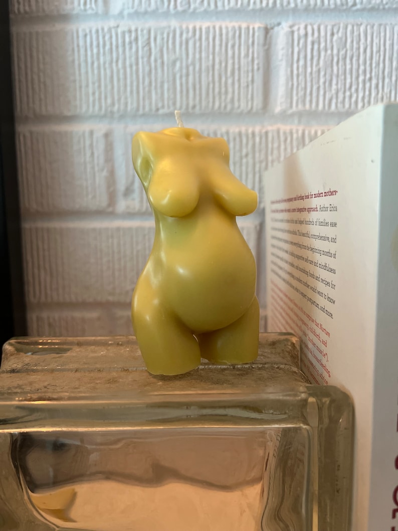 Beeswax candle in the form of a pregnant woman with belly is unlit on a birth altar, surrounded by labor books and 4th trimester support