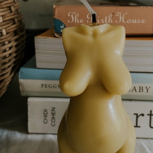 Beeswax candle in the form of a pregnant woman with big belly. Smoke from the wick is  drifting on a birth altar, surrounded by books to support mothers in childbirth