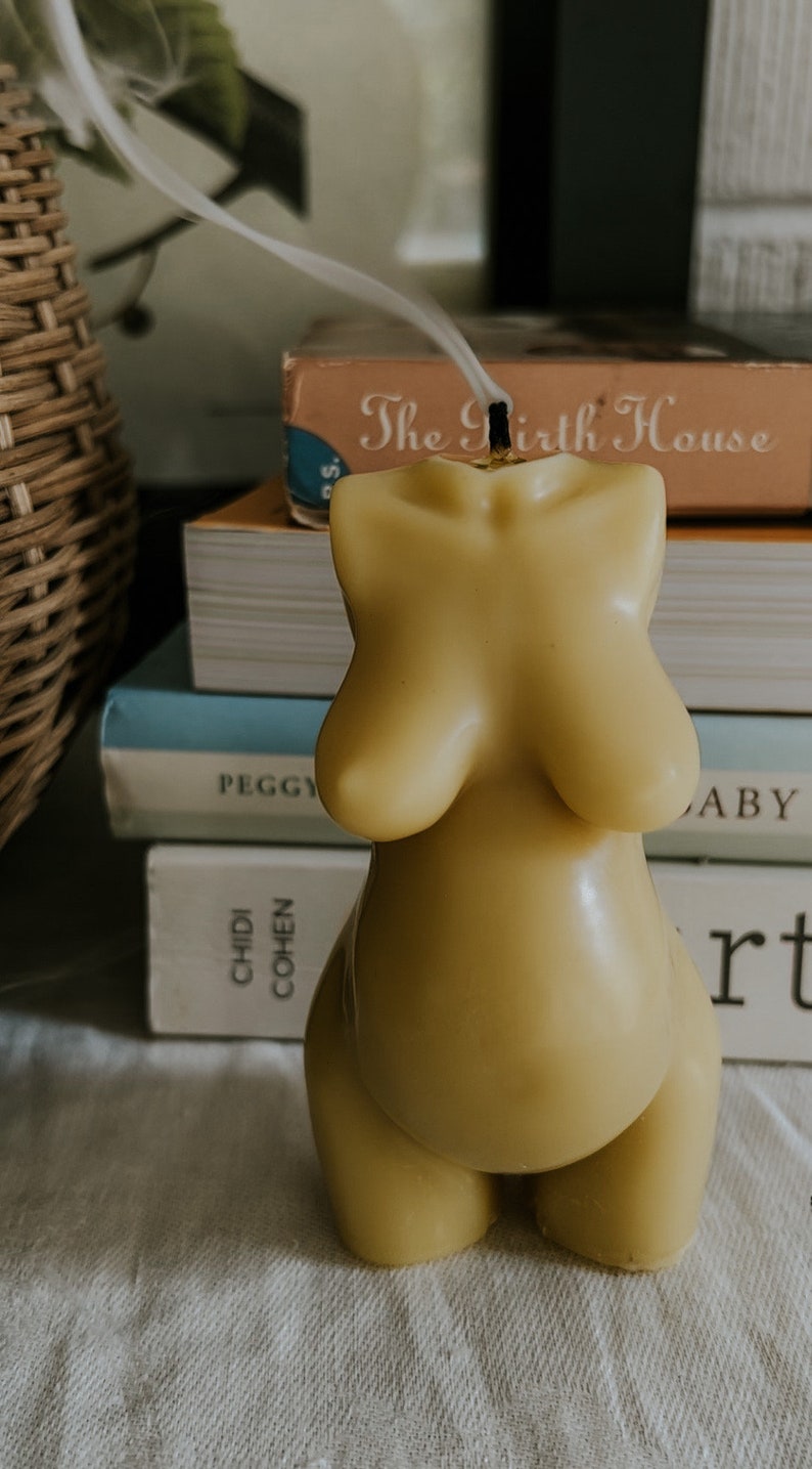 Beeswax candle in the form of a pregnant woman with big belly. Smoke from the wick is  drifting on a birth altar, surrounded by books to support mothers in childbirth