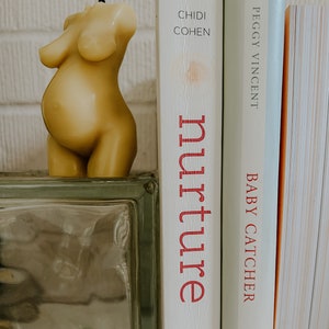 Beeswax candle in the form of a pregnant woman with belly is unlit on a birth altar, surrounded by labor books and 4th trimester support