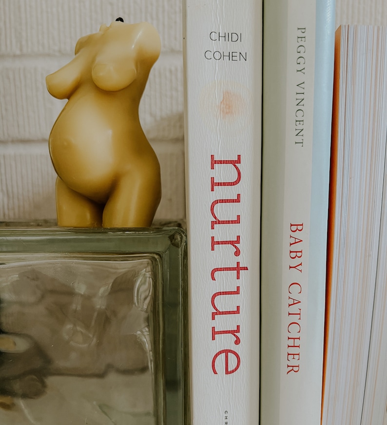 Beeswax candle in the form of a pregnant woman with belly is unlit on a birth altar, surrounded by labor books and 4th trimester support