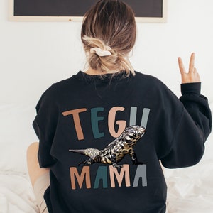 May include: Black sweatshirt with a colourful "TEGU MAMA" graphic featuring a black and white lizard.