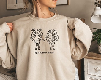 May include: A beige sweatshirt with a graphic of a heart and brain holding hands. The text "Mental Health Matters" is printed below the graphic.