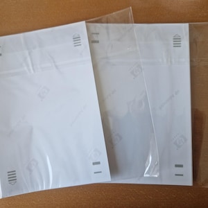 May include: Two rectangular sheets of white HP Advanced photo paper, each enclosed in a clear plastic protective sleeve. The paper features printed directional arrows and alignment markings in grey ink along the top and bottom edges of the sheets.