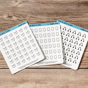 May include: Three sheets of stickers with black and white icons. The first sheet has book icons, the second sheet has e-reader icons, and the third sheet has headphone icons. Each sheet has the text "Always Plans" and a quote from Robert Louis Stevenson: "I kept always two books in my pocket, one to read, one to write in."