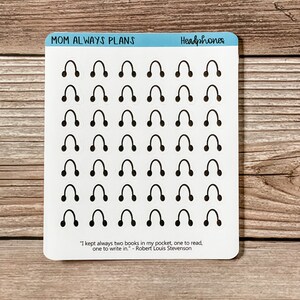 May include: A sheet of white sticker paper with 36 black headphone stickers. The stickers are arranged in 6 rows of 6. The sheet has the text "MOM ALWAYS PLANS" and "Headphones" at the top. The bottom of the sheet has a quote by Robert Louis Stevenson: "I kept always two books in my pocket, one to read, one to write in."