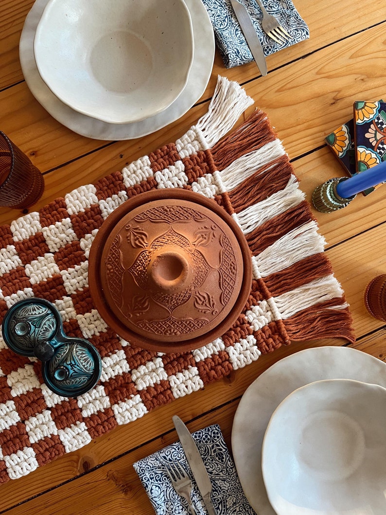 K&ouml;nnte beinhalten: Ein brauner und wei&szlig;er karierter Tischl&auml;ufer mit Fransen, ein Terrakotta-Tagine-Topf mit Deckel, zwei blaue Salz- und Pfefferstreuer aus Keramik und zwei wei&szlig;e Keramikschalen mit einem wei&szlig;en Teller unter jeder Schale.